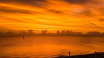 Tramonto su un corpo d'acqua calma con la silhouette di una costa in lontananza.
