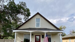A single-story house with a red door, a covered porch with red chairs, and an American flag. - G.F. Wiard House- Renovated Historic Home, Walk to Downtown Cody, Pet Friendly (Cody)