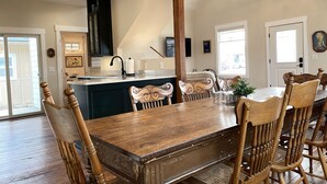 A dining area with a wooden table and chairs, a kitchen with a black cabinet, and a chandelier. - G.F. Wiard House- Renovated Historic Home, Walk to Downtown Cody, Pet Friendly (Cody)
