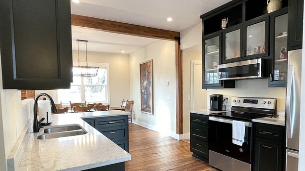 A modern kitchen with dark cabinetry, stainless steel appliances, and a wooden floor. - G.F. Wiard House- Renovated Historic Home, Walk to Downtown Cody, Pet Friendly (Cody)