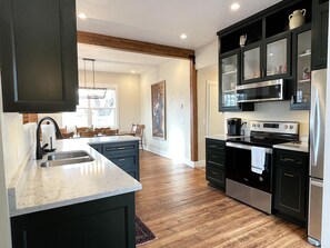 A modern kitchen with dark cabinetry, stainless steel appliances, and a wooden floor.