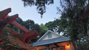 Une maison à deux étages avec un garage, une voiture blanche garée dans l’allée, et une pergola illuminée de lumières rouges.