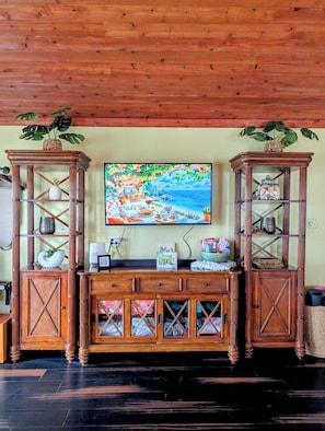 Un mueble de madera para entretenimiento con un televisor encima, flanqueado por dos aparadores con puertas de cristal, y una cesta tejida en la parte superior de cada aparador.