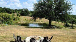 Un montaje para picnic con tres sillas y una mesa en un campo cubierto de césped, con un gran árbol y un estanque al fondo.