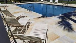 A swimming pool with lounge chairs and a tiled deck.