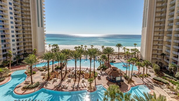 Un resort con un amplio espacio de piscina, palmeras y vista al mar.