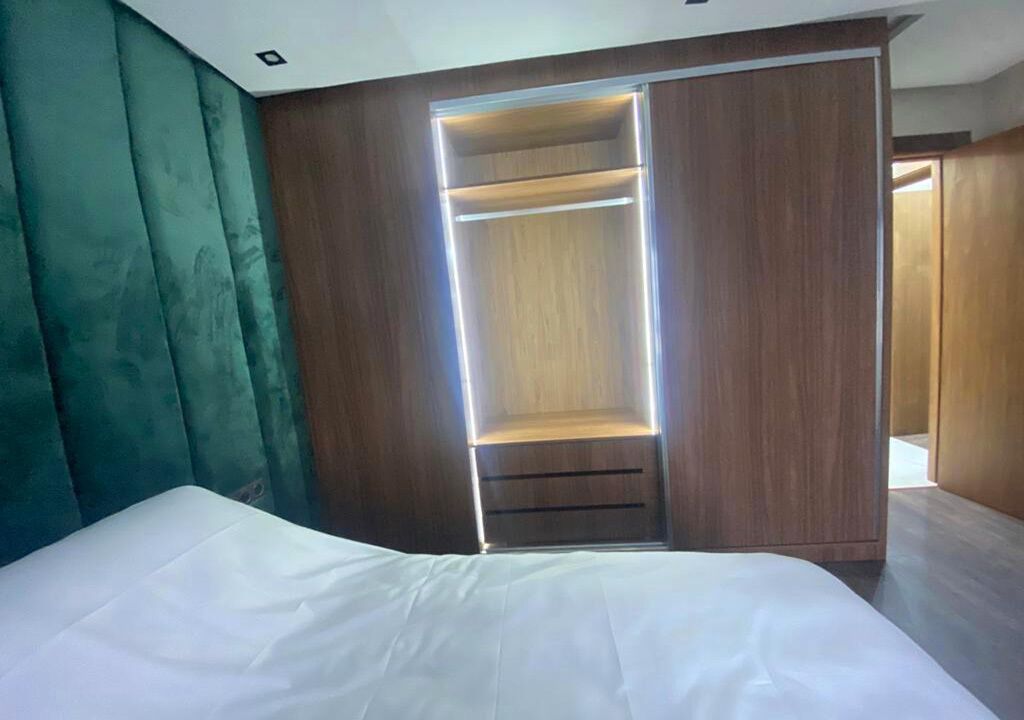 A bedroom with a bed, a wooden wardrobe with a sliding door, and a teal upholstered headboard.