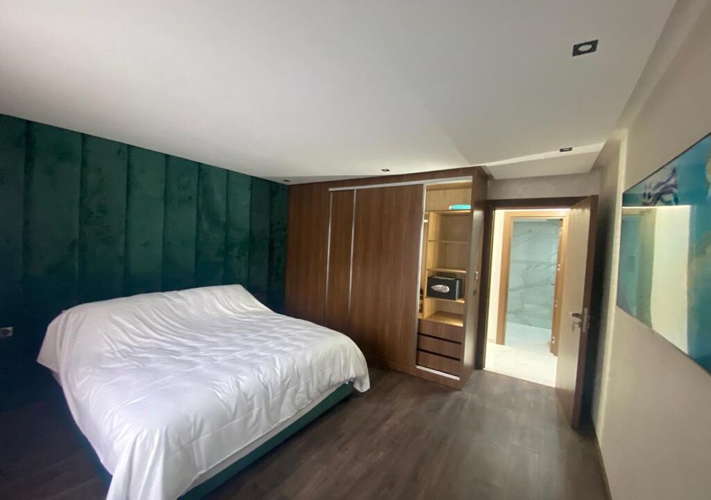 Een slaapkamer met een bed, een houten garderobe en een deur naar een andere kamer.