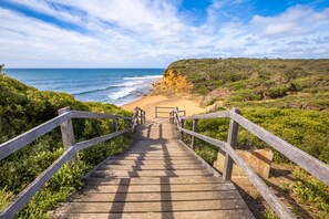 Eine Holztreppe führt zu einem Strand mit Blick auf das Meer und eine felsige Klippe.