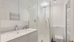 Ein modernes Badezimmer mit einer begehbaren Glasdusche, einem weißen Waschbecken und einer Toilette.