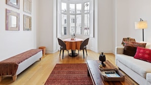 Ein Wohnzimmer mit Essbereich, einer Bank, einem Sofa, einer Lampe und Blick durch ein Erkerfenster.