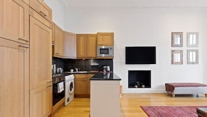 Eine moderne Küche mit Holzschränken, einer Mikrowelle und einem Einbauofen. Es gibt eine kleine Kücheninsel mit Spüle, und ein Flachbildfernseher ist an der Wand montiert.