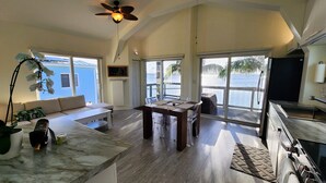 A spacious living area with a large window overlooking the sea, a ceiling fan, and a dining table with chairs.