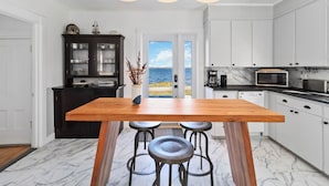 Une cuisine moderne avec une table en bois et des tabourets de bar, des meubles blancs et une vue sur la mer.