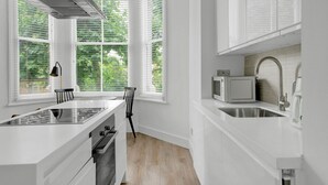 Une cuisine moderne avec des meubles blancs, une cuisinière encastrée et une fenêtre donnant sur un espace verdoyant.
