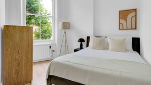 Une chambre avec un grand lit, une lampe sur pied, une fenêtre donnant sur un paysage verdoyant et une armoire en bois.