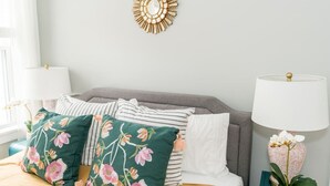 A bedroom with a bed, pillows, a wall decor piece, and a nightstand with a lamp.