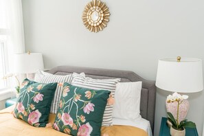 A bedroom with a bed, pillows, a wall decor piece, and a nightstand with a lamp.