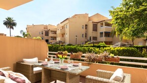 Una terraza con mobiliario de mimbre, una mesa de vidrio y plantas en macetas.