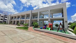 A modern building with multiple floors, large windows, and a playground area with slides and swings.