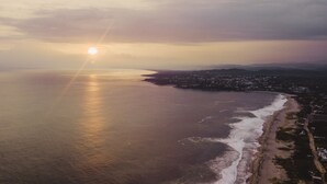 Vista aérea de una ciudad costera con playa, océano y montañas a lo lejos.