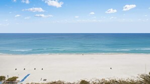 Une vaste plage de sable fin, sous un ciel bleu dégagé et une mer calme.