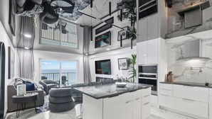 Une cuisine moderne dotée d’un îlot central, de meubles blancs et d’une grande fenêtre donnant sur l’océan.