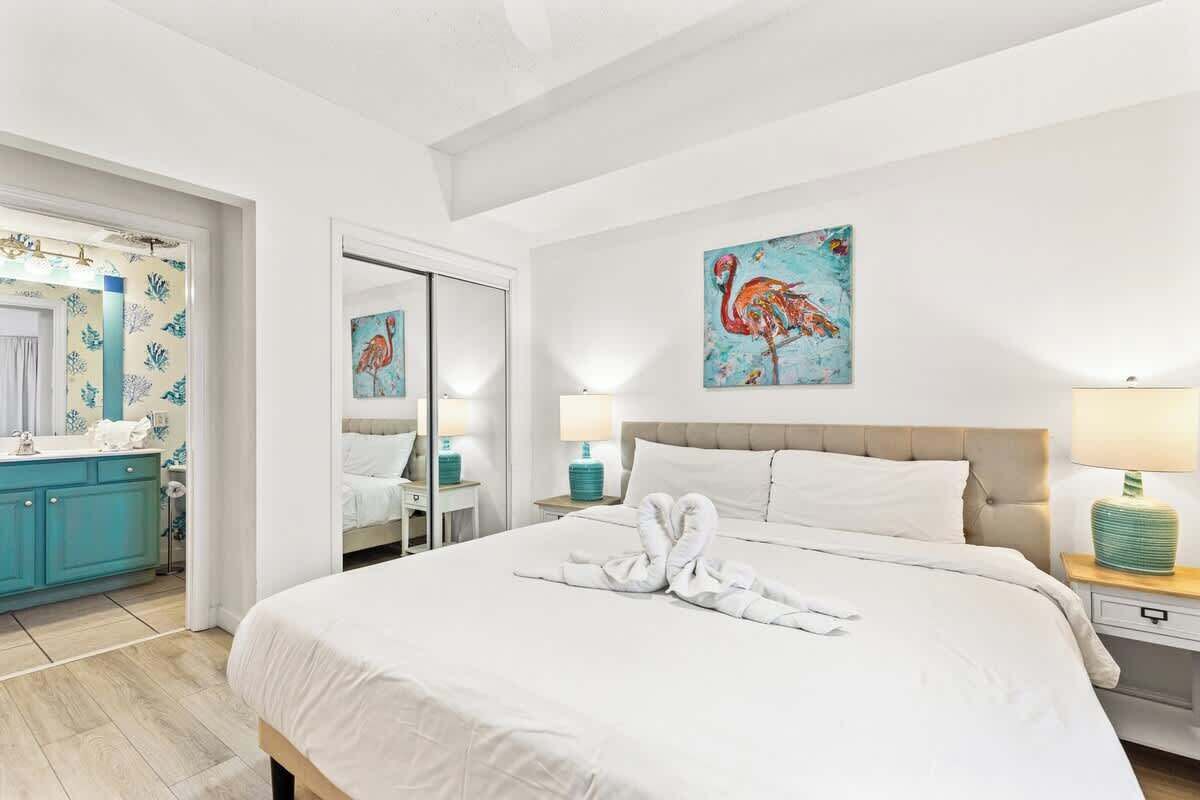 A hotel room with a large bed, a bathroom with a mirror and a toilet, and a painting of a flamingo on the wall.