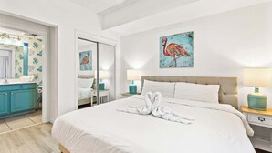 Ein Hotelzimmer mit einem großen Bett, einem Badezimmer mit Spiegel und Toilette sowie einem Flamingo-Gemälde an der Wand.