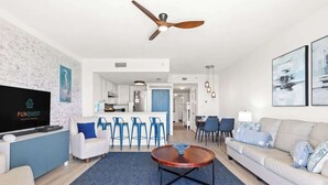 Ein modernes Wohnzimmer mit Flachbildfernseher, Deckenventilator, einer Couch, einem Couchtisch und einem Essbereich mit Stühlen.