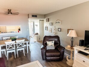 A living room with a leather armchair, a dining table with chairs, a TV stand, and a ceiling fan.