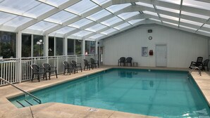 An indoor swimming pool with a glass ceiling, surrounded by chairs and a white wall with a clock. - Sea Trail 2BR - Golf, Bike, Beach Getaway! Clean, Quiet, Pools, Great View! (Sunset Beach)