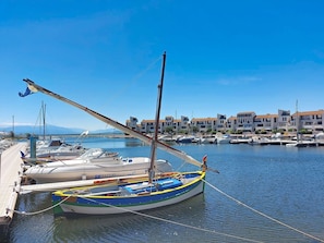 Un puerto deportivo con barcos amarrados, un muelle de madera y edificios al fondo.