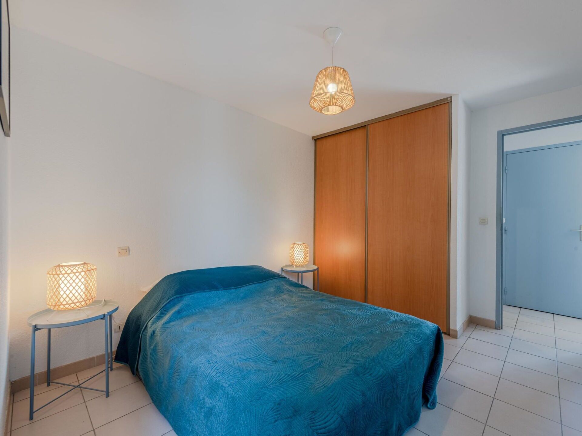 A bedroom with a bed, two bedside lamps, a wardrobe, and a door.