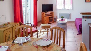 A dining area with a table set for two, a television, and a small table with a plant.