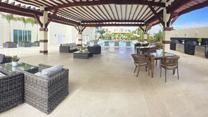 Eine Außenpatio-Terrasse mit Korbmöbeln, einem Pool und einem überdachten Sitzbereich.