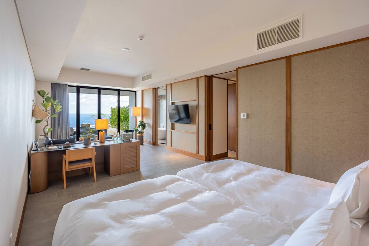 A hotel room with a large bed, a desk with a chair, a TV, and a view of the outdoors.