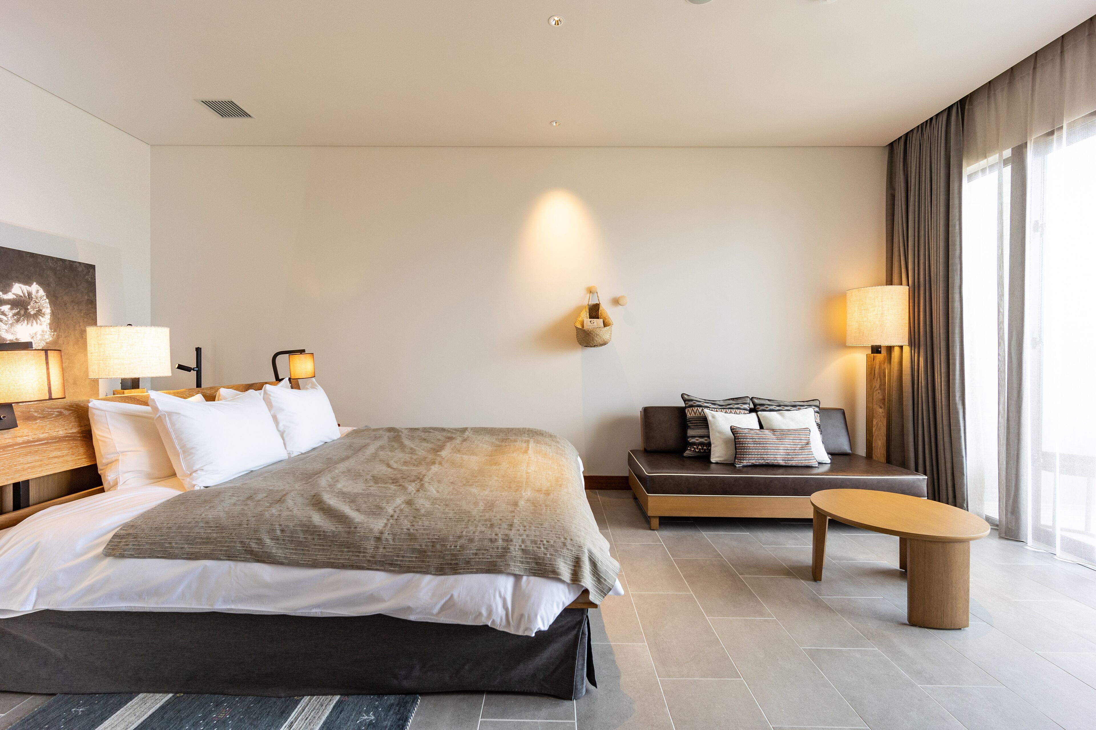 A modern hotel room with a large bed, bedside lamps, a sofa, and a small table.