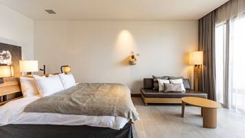 A modern hotel room with a large bed, bedside lamps, a sofa, and a small table.