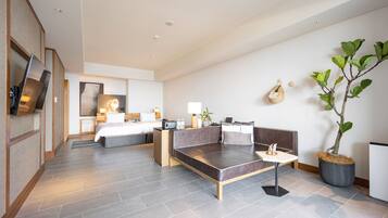 A modern hotel room with a large bed, a sofa, a small table, and a potted plant.