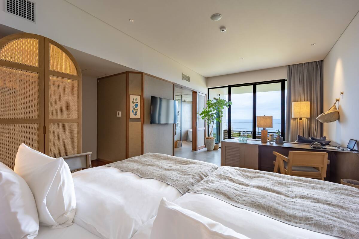 A hotel room with a large bed, a desk, a chair, a TV, and a view of the outdoors.