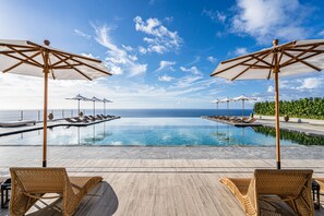 A poolside area with lounge chairs and umbrellas, overlooking a clear blue sky and ocean. - One Suite THE GRAND (Nakijin)