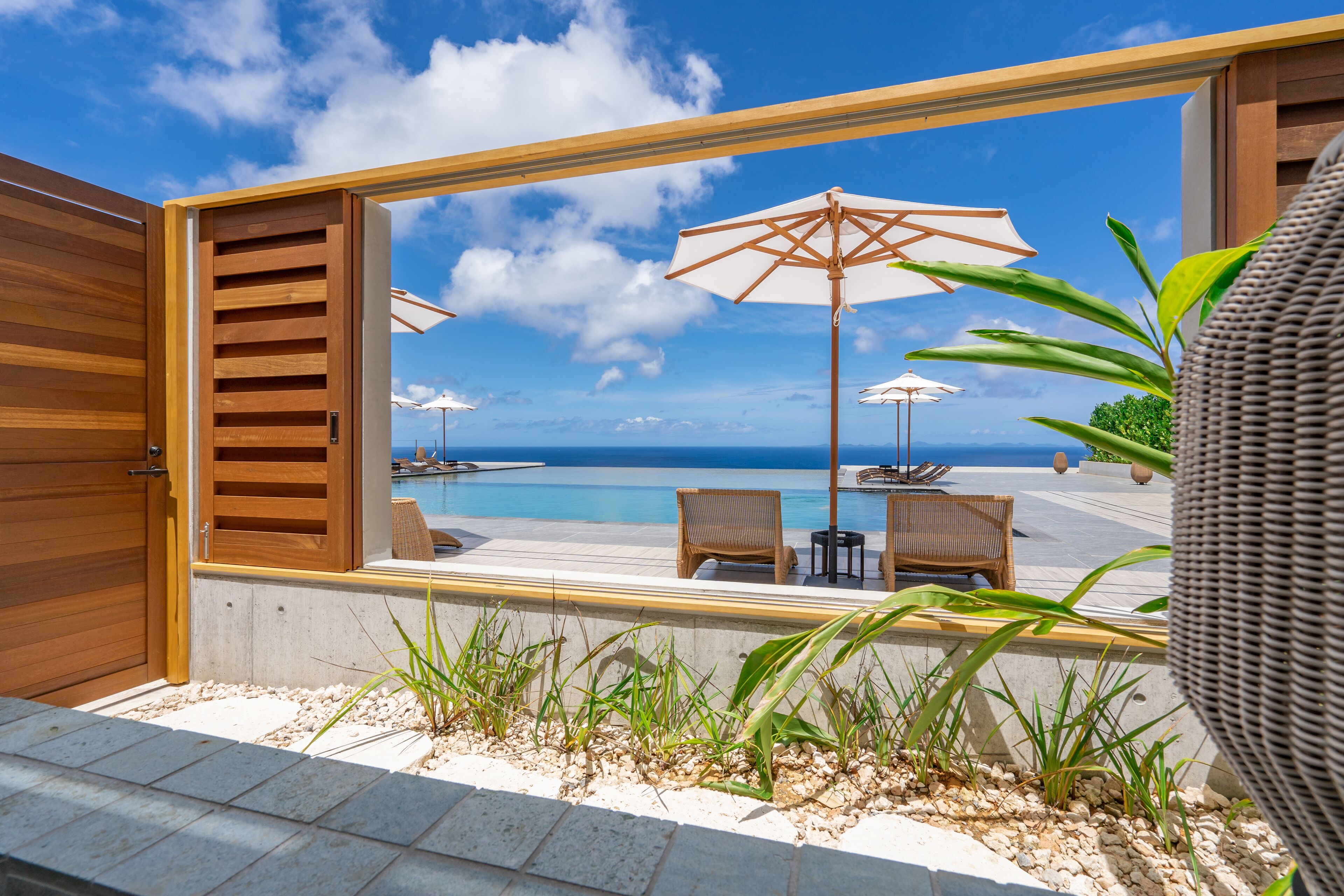 A modern outdoor seating area with a pool view, wooden shutters, and outdoor umbrellas.