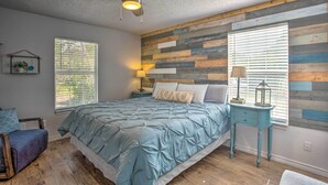 Una camera da letto con un letto, un comodino, una sedia, una ventola a soffitto e una parete con decorazioni in legno.