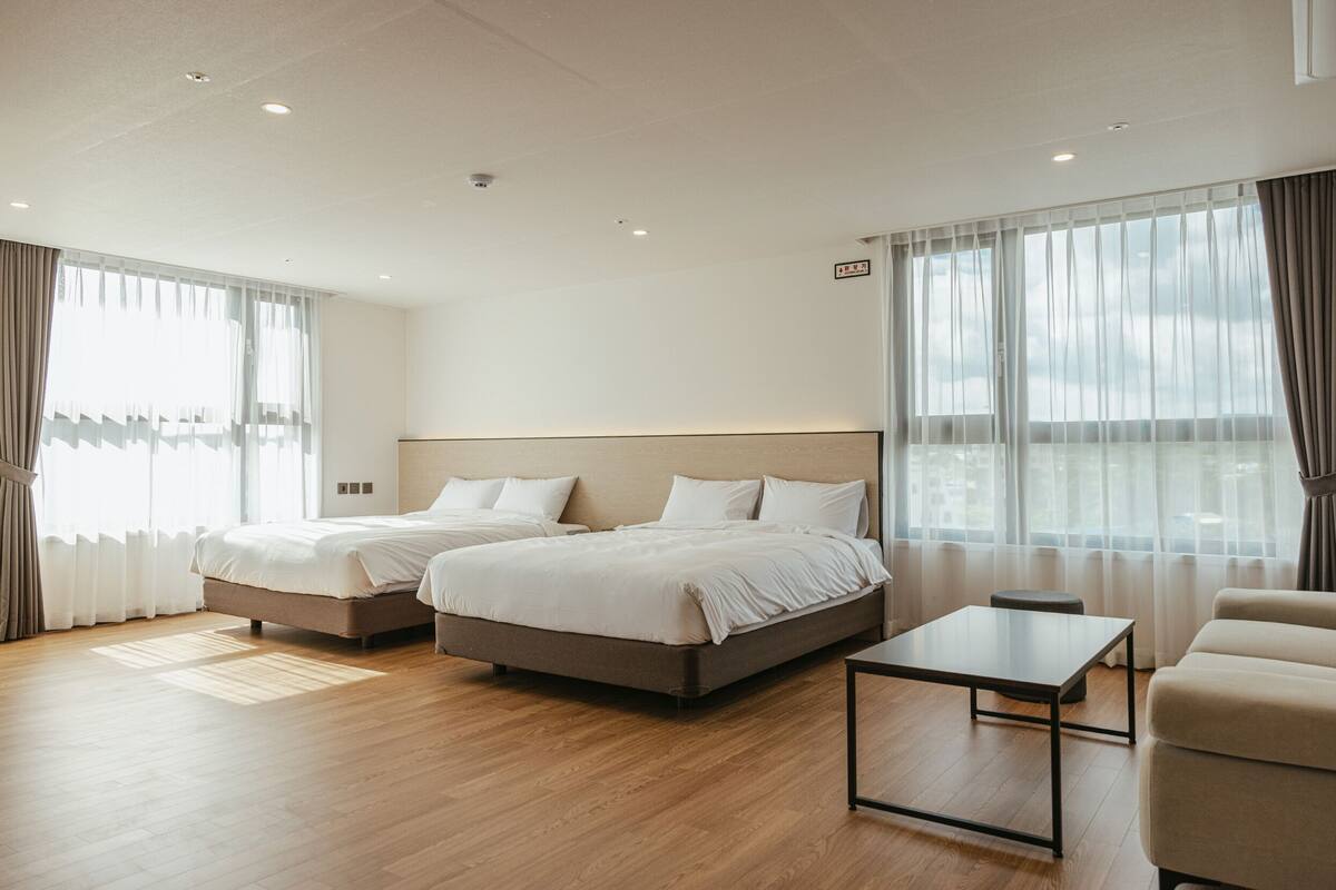 Une chambre d’hôtel avec deux lits, un canapé, une petite table et de grandes fenêtres avec des rideaux.