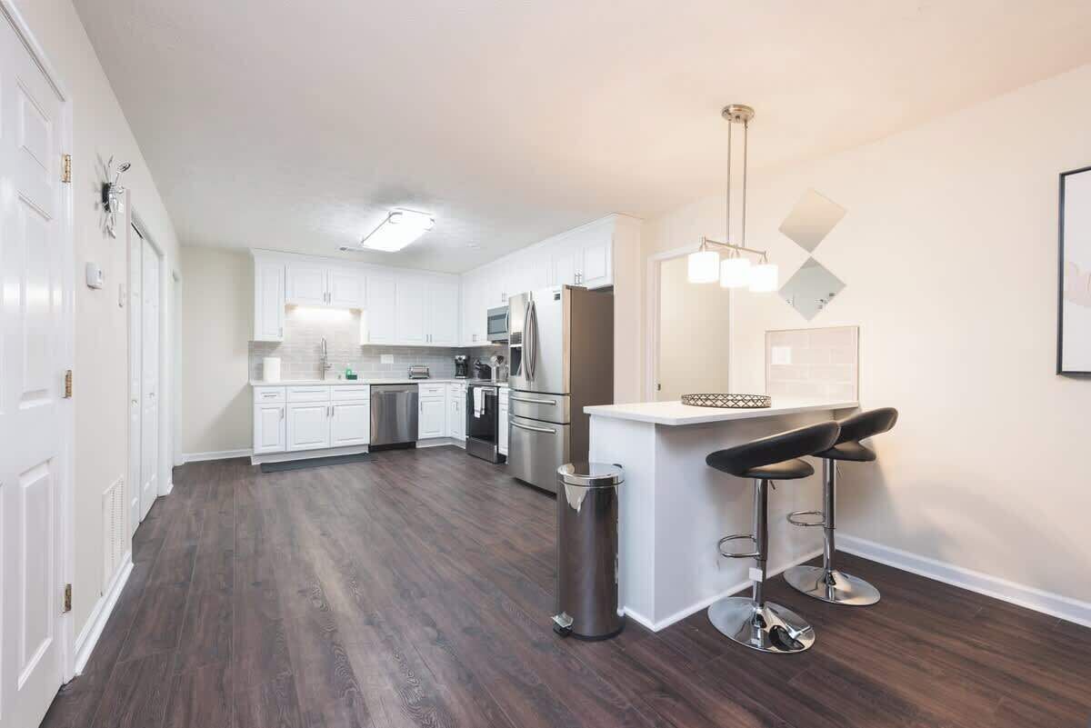 A modern kitchen with white cabinets, stainless steel appliances, and a bar area with stools.