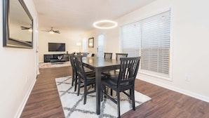 A dining area with a rectangular table, six chairs, a ceiling fan, and a large mirror on the left wall.