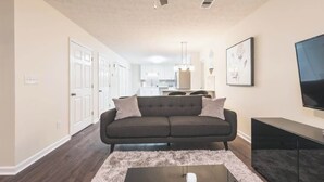 A living room with a dark sofa, a flat-screen TV, and a ceiling fan.