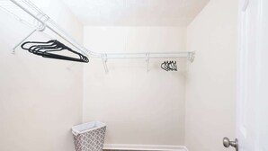 A small, enclosed room with a wooden floor, a white door, and a metal rack with clothes hanging.