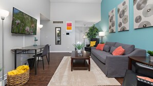 A modern living room with a flat-screen TV, a dining table with chairs, a gray sofa with red cushions, and a coffee table.